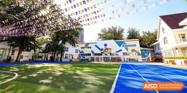 The colorful exterior of a school building with a well-maintained green lawn and playground at Yew Chung International School of Beijing.