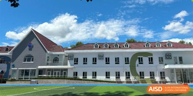 The exterior of a white, stately school building with a green lawn and blue sky at Yew Chung International School of Beijing.