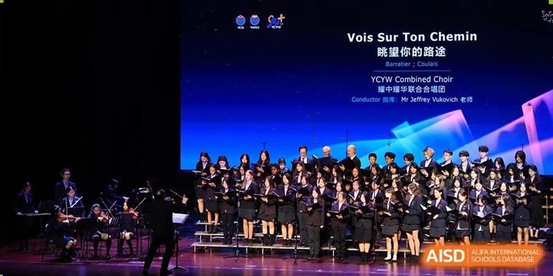 A large student choir or performance group singing on a dark stage during a school event at Yew Chung International School of Beijing.