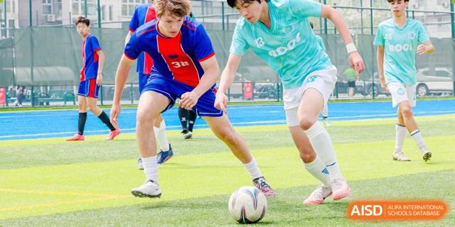 Close-up of students' legs and feet playing rugby or football on a blue turf field at Yew Chung International School of Beijing.