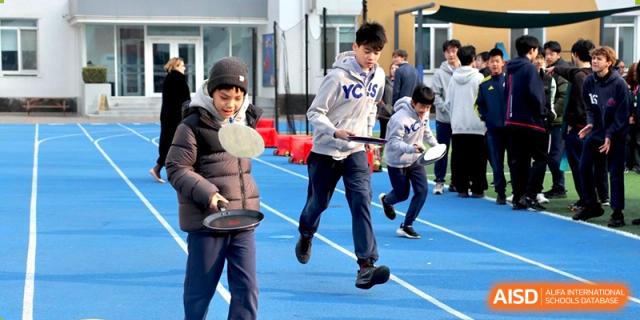 Students playing a game like paddleball or badminton on a blue outdoor court at Yew Chung International School of Beijing.