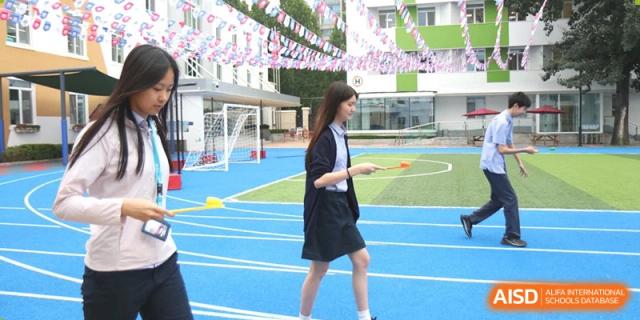 A student in a school uniform walking on a blue track or sports area under festive decorations at Yew Chung International School of Beijing.