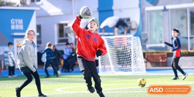 A young student in a red uniform running with a ball near a goal net at Yew Chung International School of Beijing.