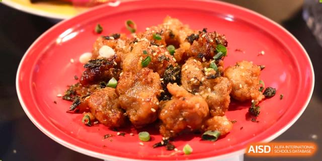 A serving of dark, crispy, glazed chicken, sprinkled with sesame seeds, served on a red plate at Yew Chung International School of Beijing.