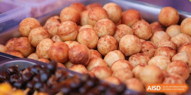 A close-up of a pile of golden-brown, bite-sized fried dough balls or savory puffs at a food service event at Yew Chung International School of Beijing.