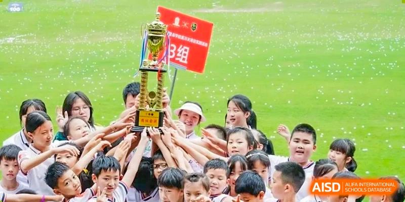 A large group of children and students celebrating a victory while holding a large golden trophy high in the air at Maple Leaf International School Chongqing.