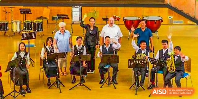 An image of an adult orchestra or band performing with various instruments and a conductor, possibly during a school concert at Maple Leaf International School Chongqing.