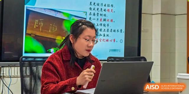 A teacher leading a discussion or presenting material from a projection screen in a classroom at Wuxi Big Bridge Academy.