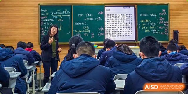 Students taking notes and focusing on a blackboard with complex Chinese text during a lecture at Wuxi Big Bridge Academy.