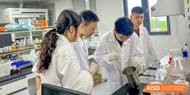 Two students in lab coats stirring a mixture during a group science experiment at Wuxi Big Bridge Academy.