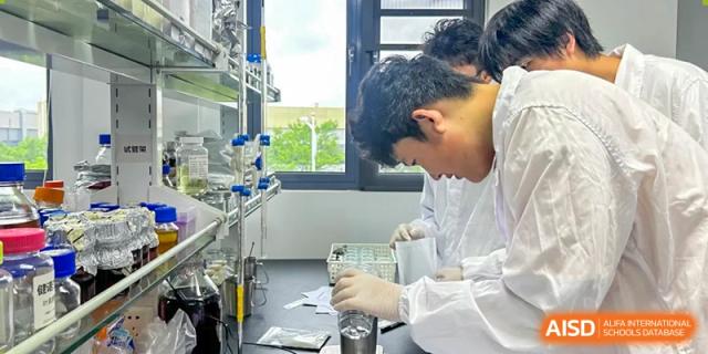 A student wearing a lab coat and gloves meticulously conducting a chemistry experiment using glassware in a science laboratory at Wuxi Big Bridge Academy.