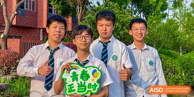Two male students posing outdoors, one holding a sign that says "Youth is the Time" (青春正当时), at Wuxi Big Bridge Academy.