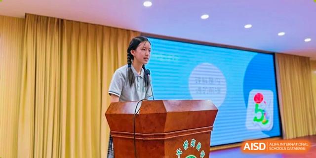 A female student giving a speech at a wooden podium in an assembly hall at Wuxi Big Bridge Academy.