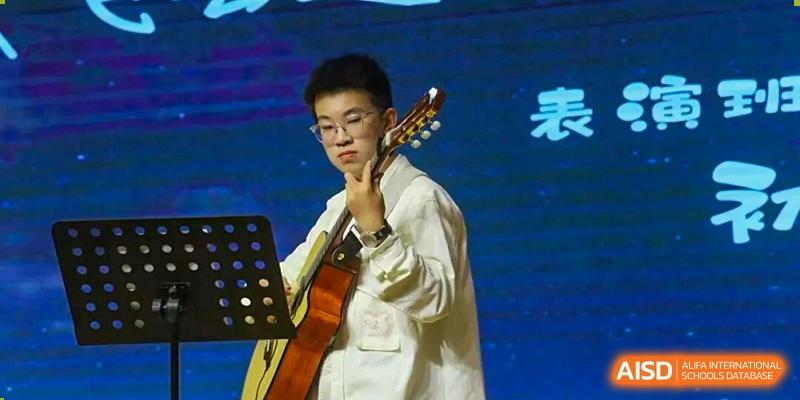 A male student playing an acoustic guitar and singing on stage during a performance at Wuxi Big Bridge Academy.