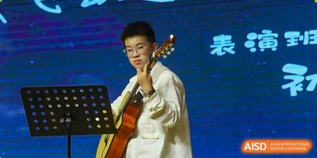 A male student playing an acoustic guitar and singing on stage during a performance at Wuxi Big Bridge Academy.