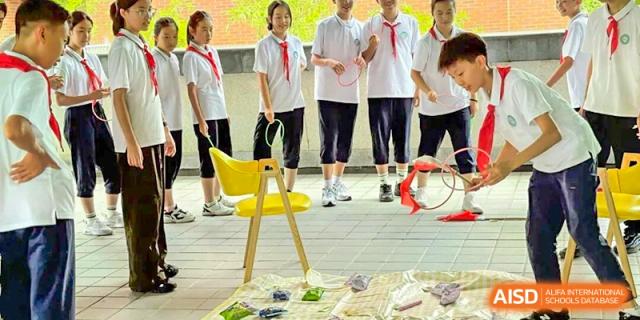 Students in red scarves participating in an outdoor activity or practical lesson at Wuxi Big Bridge Academy.