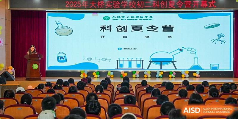 Students attending a lecture or presentation in an auditorium, with a screen displaying academic content at Wuxi Big Bridge Academy.