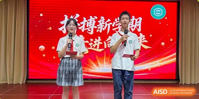A male student speaking confidently into a microphone on stage during a public speaking event or ceremony at Wuxi Big Bridge Academy.