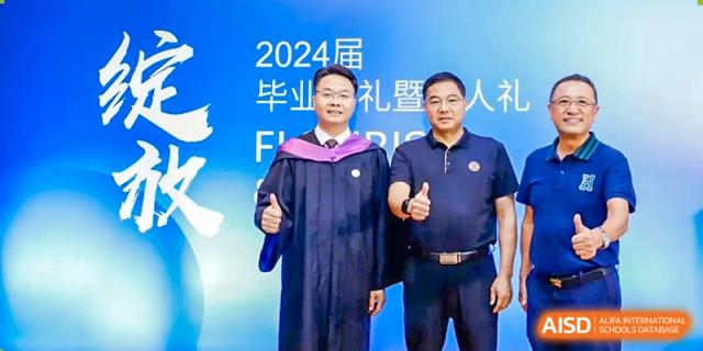 The principal and another male staff member from Zhuhai Oriental Yinghua International Academy posing in front of a banner for the 2024 graduation ceremony.