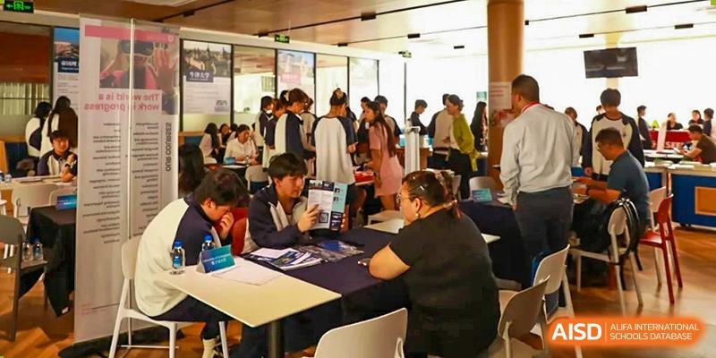 Students and staff gathered at tables during an event at Zhuhai Oriental Yinghua International Academy, likely a college admissions fair.