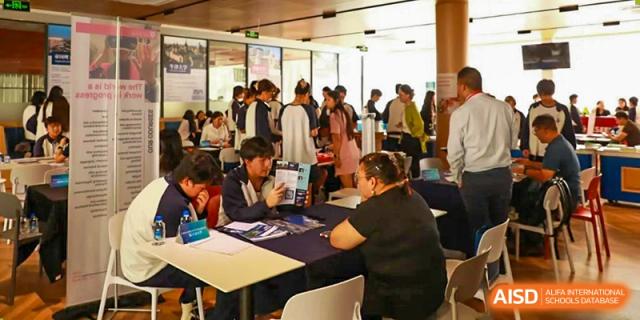 Students and staff gathered at tables during an event at Zhuhai Oriental Yinghua International Academy, likely a college admissions fair.
