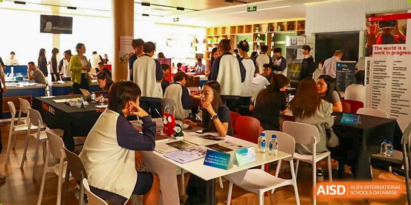 A busy scene at the Zhuhai Oriental Yinghua International Academy graduation or university fair, with people gathered around tables.