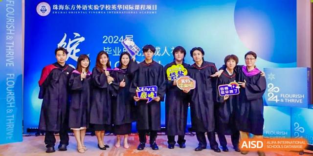 A group of Zhuhai Oriental Yinghua International Academy students in graduation gowns posing together for a photo.