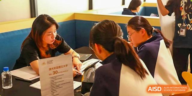 A female student from Zhuhai Oriental Yinghua International Academy interacting with a representative at a recruitment table.