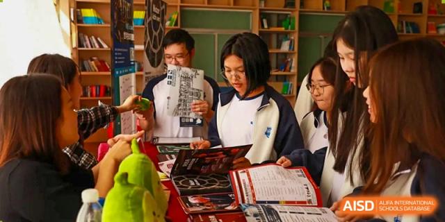 A female student from Zhuhai Oriental Yinghua International Academy reviewing pamphlets at a college admissions booth.