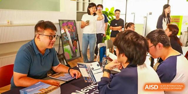 Students from Zhuhai Oriental Yinghua International Academy discussing or reviewing materials at a college fair booth.