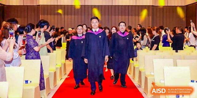 A row of graduates from Zhuhai Oriental Yinghua International Academy walking down an aisle in their gowns.