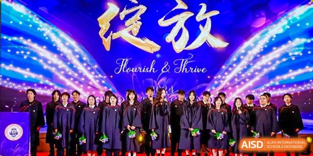 A group of graduates from Zhuhai Oriental Yinghua International Academy in gowns standing beneath a banner that reads "Flourish & Thrive."