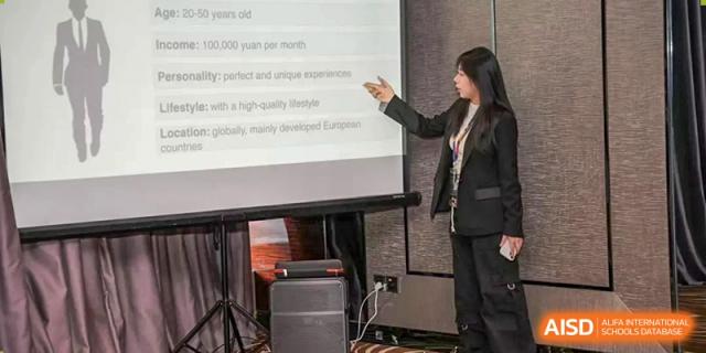 A female staff member or presenter from Zhuhai Oriental Yinghua International Academy pointing to text on a large projection screen.