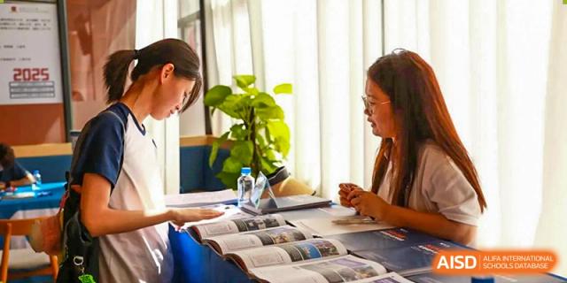 Two students from Zhuhai Oriental Yinghua International Academy and an adult reviewing open books or materials at a table with a plant.
