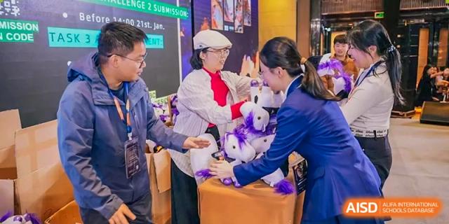 A student from Zhuhai Oriental Yinghua International Academy receiving a promotional item at a booth with a staff member dressed in white.