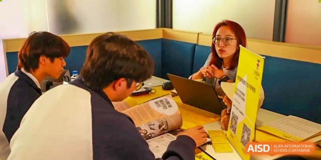 Two students from Zhuhai Oriental Yinghua International Academy studying or working on a laptop together in a casual study area.