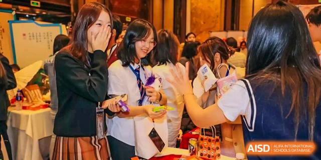 A female student from Zhuhai Oriental Yinghua International Academy smiling and interacting with others at a school event or fair.
