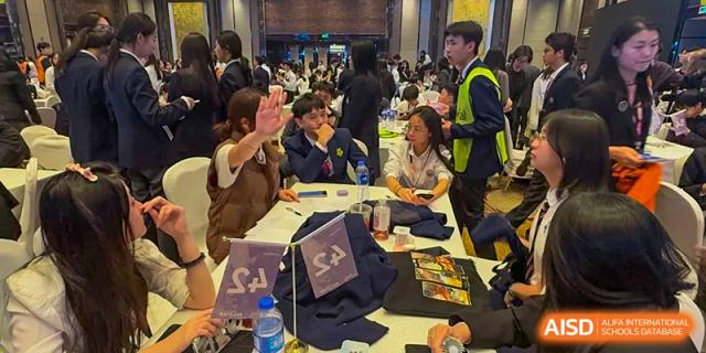 A busy scene with students and staff from Zhuhai Oriental Yinghua International Academy seated at tables during a large event or fair.