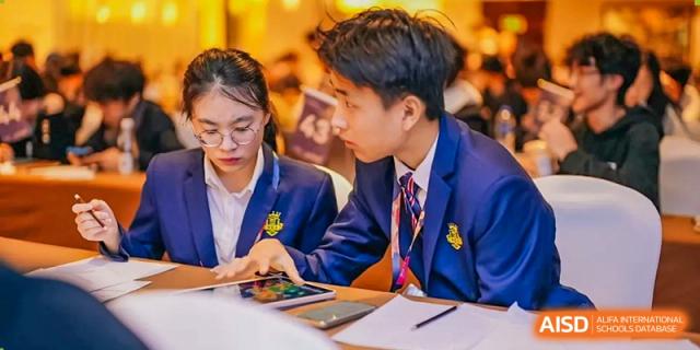 Two students from Zhuhai Oriental Yinghua International Academy reviewing papers together at an event table.