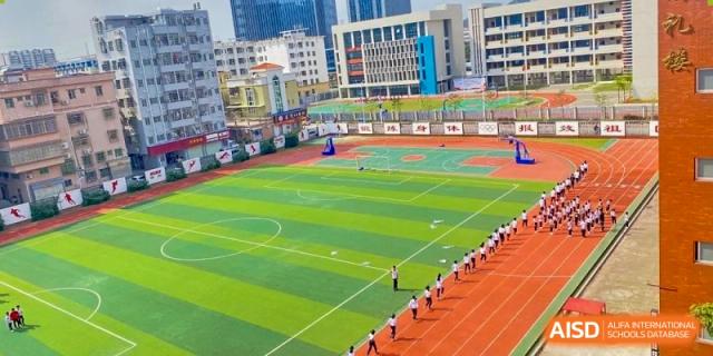 An aerial view of the sports field at Zhuhai Oriental Yinghua International Academy, showing a running track, green field, and students in formation.