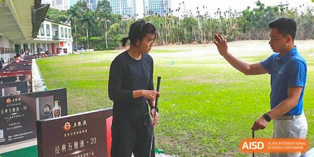 A male student from Zhuhai Oriental Yinghua International Academy holding a golf club at an outdoor driving range.