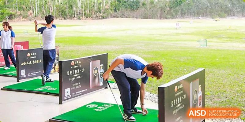 A student from Zhuhai Oriental Yinghua International Academy bending over to adjust a golf ball on a tee at a driving range.