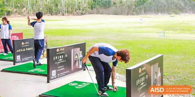 A student from Zhuhai Oriental Yinghua International Academy bending over to adjust a golf ball on a tee at a driving range.