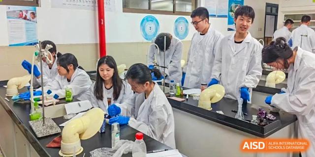 Students in white lab coats are gathered around a workbench, carefully using laboratory tools and chemicals for an experiment in a science classroom at Changjun Bilingual School Of Changsha City.