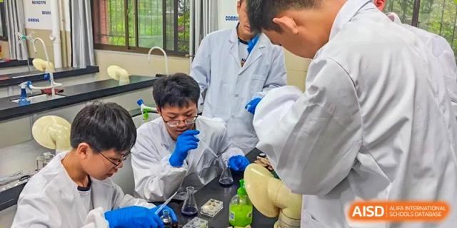 A close-up view of two students wearing blue gloves and safety goggles working on a science experiment with various flasks and liquids in a lab at Changjun Bilingual School Of Changsha City.