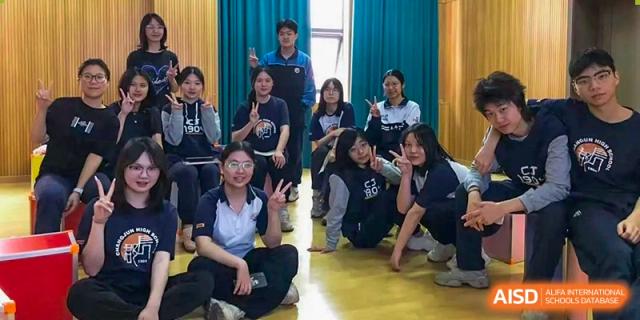 A group of happy students from Changjun Bilingual School Of Changsha City posing together for a fun photo indoors, some making peace signs.