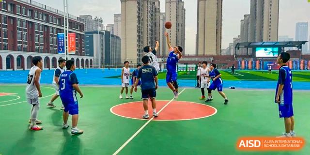 A mid-range view of students from Changjun Bilingual School Of Changsha City playing basketball on a green and blue outdoor court.