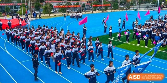 A large group of students from Changjun Bilingual School Of Changsha City in uniform participating in an organized outdoor event on a track.