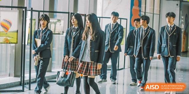 Two students from Cogdel Cranleigh High School, dressed in dark uniform jackets and plaid skirts, walking indoors.