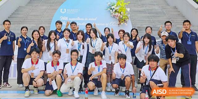 A group of students from Cogdel Cranleigh High School, dressed in school uniforms and casual wear, posing for a group photo at an outdoor event with a floral backdrop.